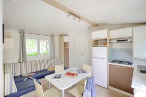 A compact room with a dining table, a bench, a kitchenette, and a window with curtains. - Camping 4 étoiles - Piscine  - ccbggc0 (Cordelle)