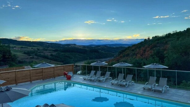 Ein Swimmingpool mit Liegestühlen und Sonnenschirmen, umgeben von einem Holzzaun, mit Blick auf ein Tal.