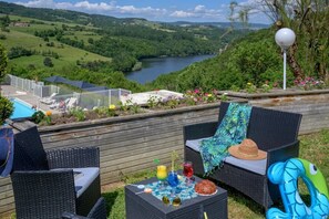 Eine Terrasse mit Korbmöbeln, einem Tisch mit Getränken und Blick auf einen See und Hügel.