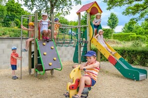 Kinder spielen auf einem Spielplatz mit Rutsche und Klettergerüsten.