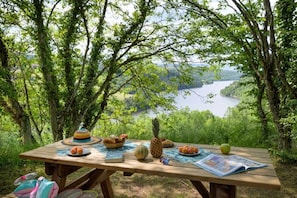 A picnic table set outdoors with a view of a lake and forest.