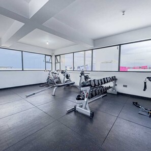 Et fitnesscenter med træningsudstyr, store vinduer og højt til loftet.