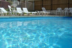 En pool med kristallklart vatten och vita solstolar längs kanten.