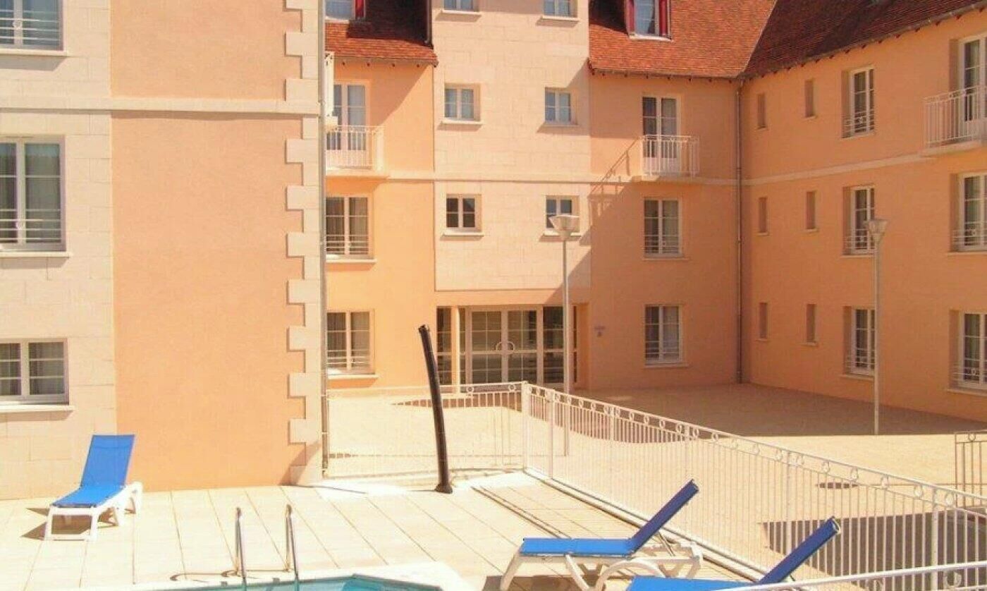 A multi-story building with balconies, a swimming pool, and lounge chairs.