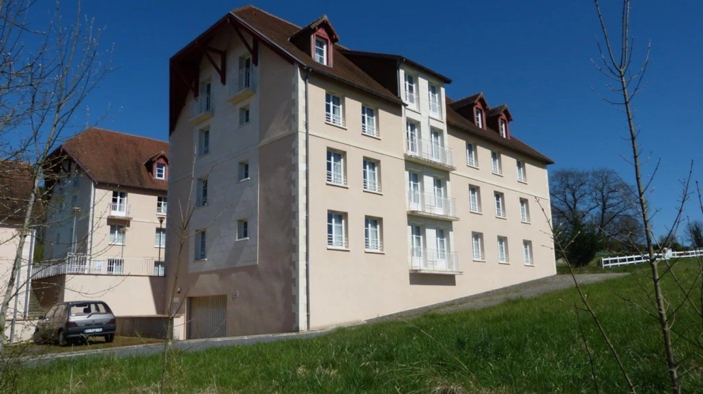 A multi-story residential building with balconies, a car parked in front, and a grassy slope.
