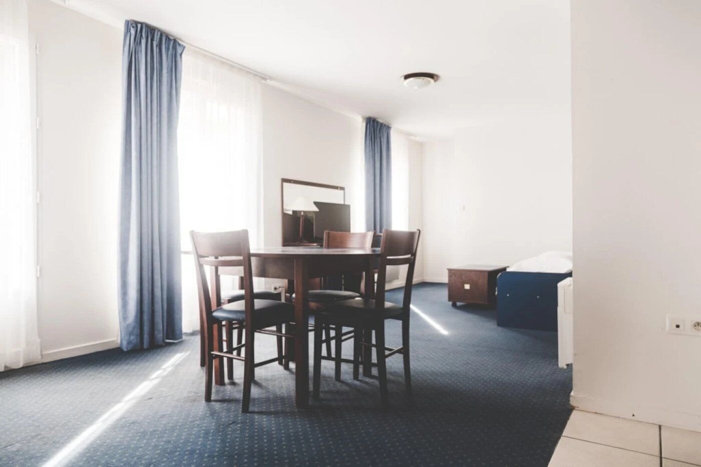 A hotel room with a dining table, chairs, a small cabinet, and a bed.