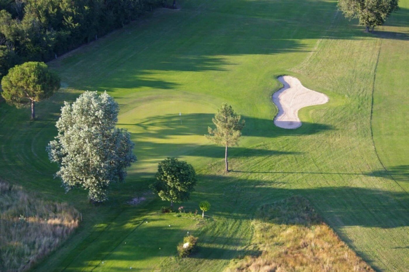 An aerial view of a golf course with a sand bunker, trees, and well-maintained grass.