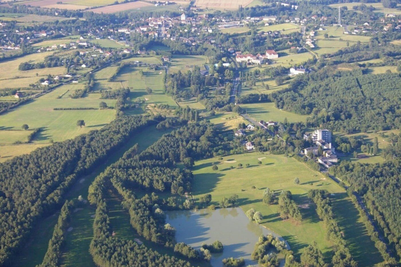 Une vue aérienne d’une zone rurale avec une rivière, des champs et quelques bâtiments dispersés.