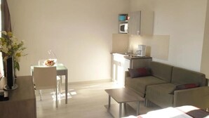 A modern living room with a sofa, a dining table, and a kitchen area with a microwave. - Appartement 3 étoiles - ccbgfdd (Allevard)