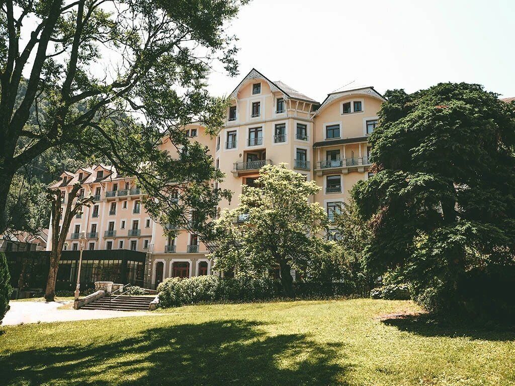 A multi-story hotel with a central courtyard, surrounded by lush greenery and trees.