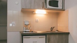 A compact kitchen with a built-in microwave, a small refrigerator, and a shelf above the sink. - Appartement 3 étoiles - ccbgfdf (Allevard)
