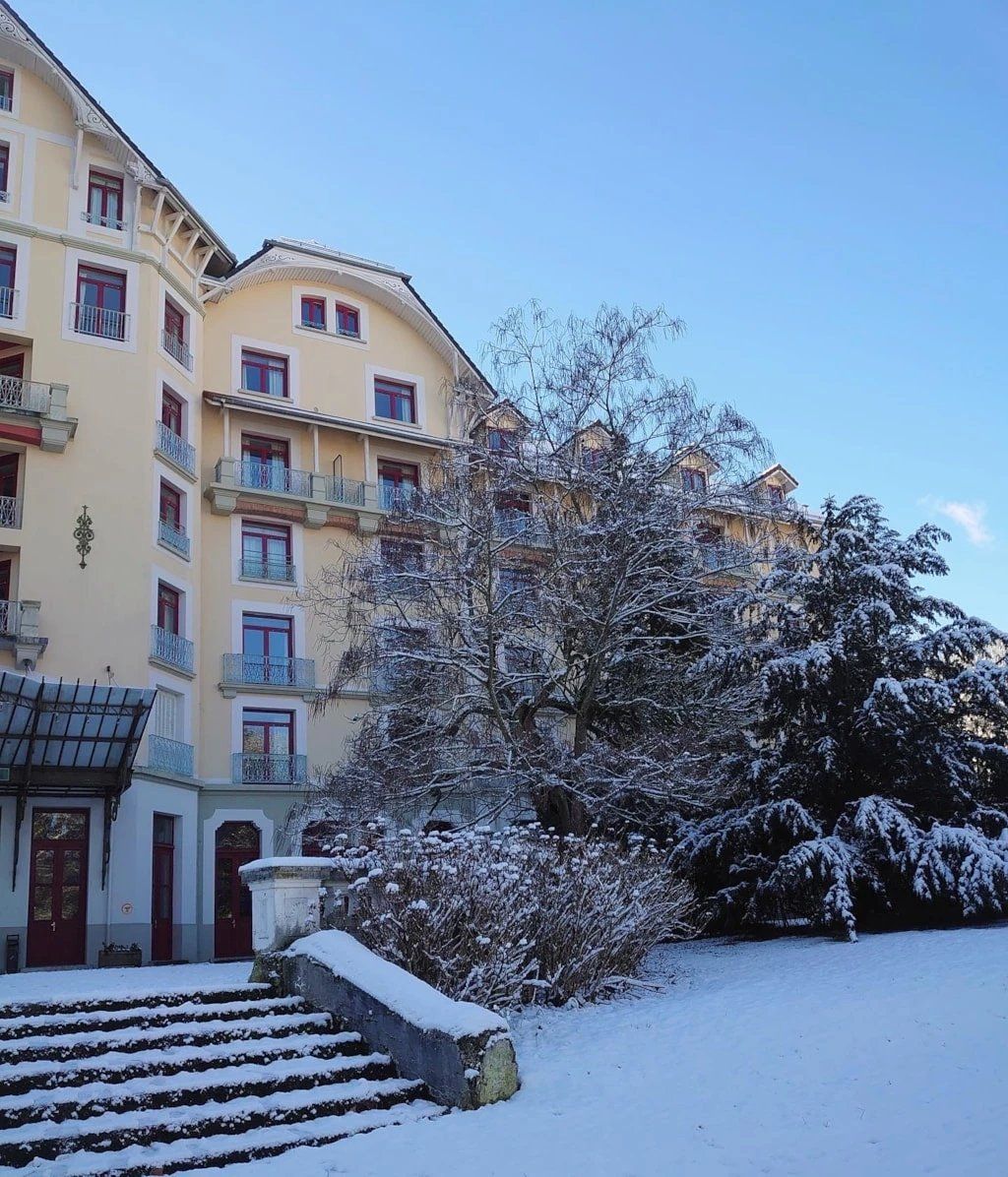 A multi-story building with balconies, a snow-covered entrance, and a clear sky.