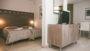 Ein Hotelzimmer mit zwei Betten, einem Fernseher auf einem Schrank, einem Schreibtisch und einem Sessel.