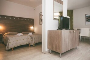 Ein Hotelzimmer mit zwei Betten, einem Fernseher auf einem Schrank, einem Schreibtisch und einem Sessel.