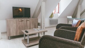Ein Loft-Zimmer mit Fernseher auf einer Holzkabine, einem kleinen Tisch mit Fernbedienung, Korbmöbeln und einem Fenster mit Blick.