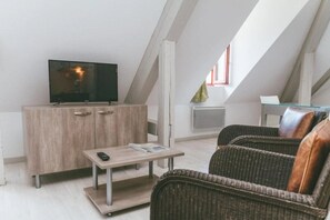 Ein Loft-Zimmer mit Fernseher auf einer Holzkabine, einem kleinen Tisch mit Fernbedienung, Korbmöbeln und einem Fenster mit Blick.