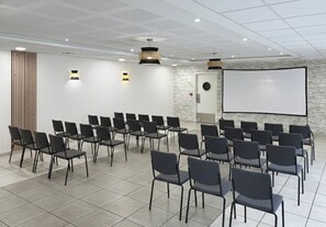 Un salón de conferencias con hileras de sillas, una pantalla de proyector y una pizarra.