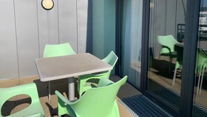 Um pátio com mesa e cadeiras, uma porta de correr com vidro e um aparelho de luz fixado na parede.
