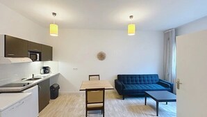 Ett kompakt bostadsutrymme med ett litet kök, ett matbord, en soffa och ett litet soffbord.