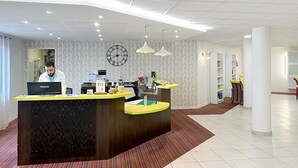 A reception desk with a clock, a computer, and a counter with a yellow top. - Appartement 3 étoiles - ccbgffh (Rouen)
