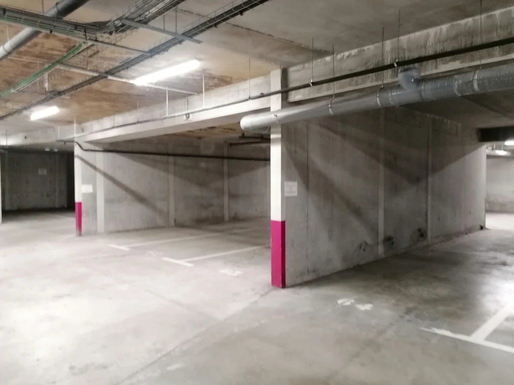 An empty parking garage with concrete pillars and overhead pipes.
