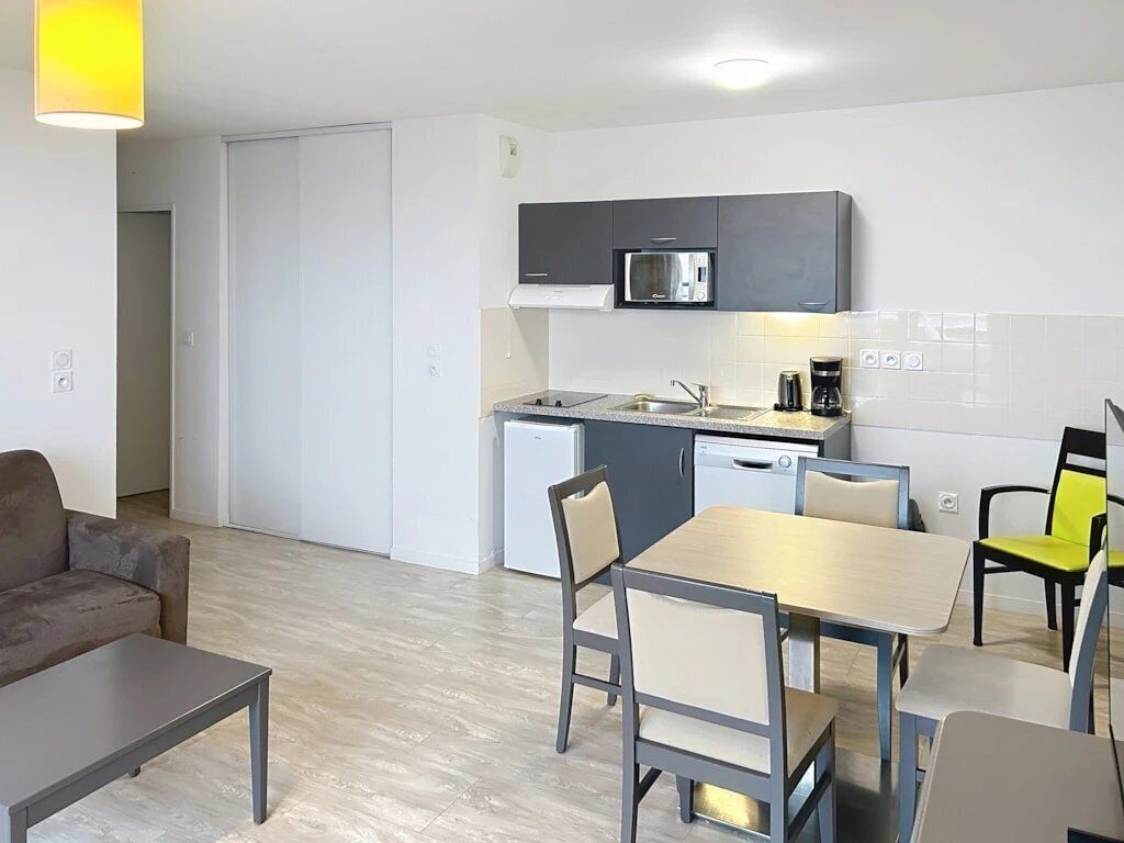 Een ruimtelijke leefruimte met een kitchenette, een eethoek en een bank.