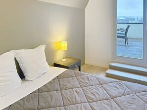 A bedroom with a bed, a nightstand with a lamp, and a window with a view of a chair and a body of water. - Appartement 3 étoiles - ccbgffi (Rouen)