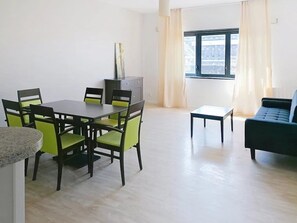 Un comedor con una mesa y sillas, un sofá, un ventanal con cortinas y un radiador.