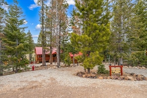 A lodge with a red roof, surrounded by trees and a gravel path. - The Office With Hot Tub and Dogs OK (Duck Creek Village)