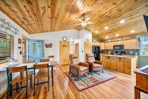 A cozy interior with a wooden ceiling, a dining area with chairs, a sofa, a kitchen with wooden cabinets, and a clock on the wall. - The Office With Hot Tub and Dogs OK (Duck Creek Village)