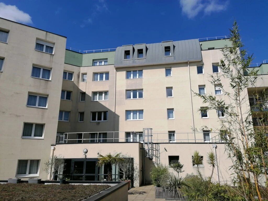 A multi-story building with a flat facade, large windows, and a small outdoor area with plants.