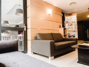 Ein modernes Wohnzimmer mit einem grauen Sofa, einem Couchtisch und einem Bücherregal voller Zeitschriften.
