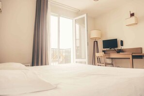 Ein Hotelzimmer mit einem Bett, einem Schreibtisch mit Computer, einer Lampe und einem Fernseher.