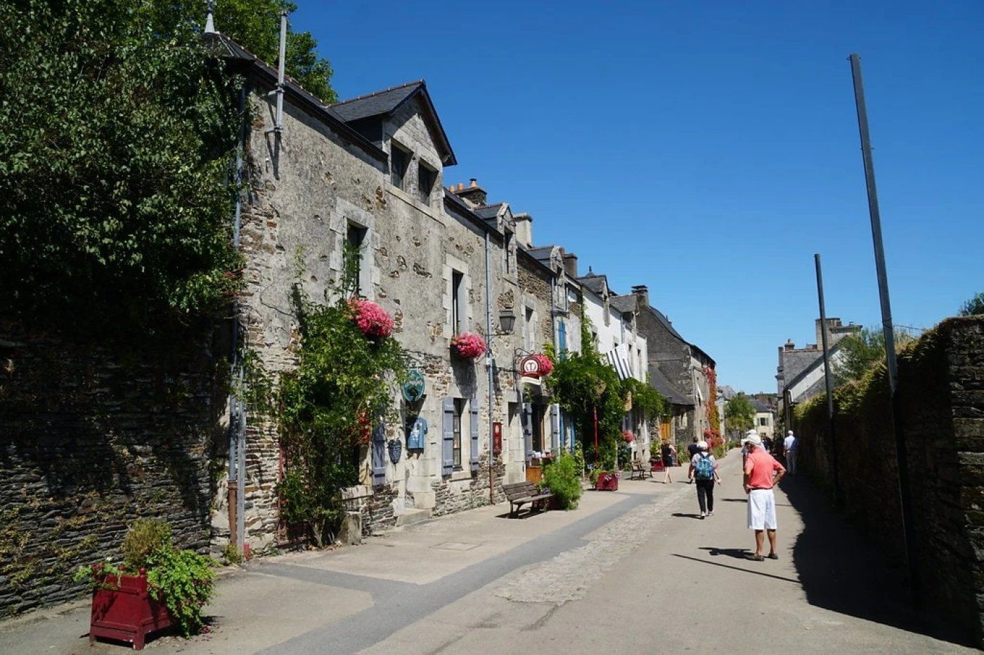 Una calle estrecha flanqueada por edificios de piedra, algunos adornados con macetas y contraventanas.