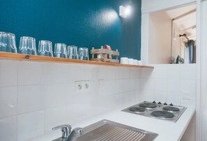 A kitchen with white tiles, a stove, and a blue wall. - Camping 2 étoiles - Piscine  - ccbgfec (Pluherlin)