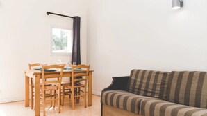 Ein Zimmer mit Esstisch für vier Personen, einer Couch, einem Fenster mit Vorhang und einer Wandleuchte.