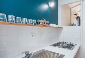A kitchen with white tiles, a stove, and a blue wall. - Camping 2 étoiles - Piscine  - ccbgfed (Pluherlin)