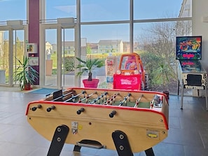 Dans le hall, on trouve une table de baby-foot, de grandes fenêtres, une borne d’arcade rouge et un écran de télévision qui diffuse un jeu.
