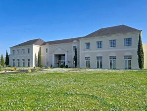 Un grand bâtiment à deux étages, doté d’une façade symétrique, d’une entrée centrale et d’une pelouse bien entretenue agrémentée de fleurs blanches.