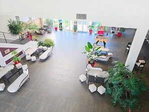 Eine geräumige Lobby mit mehreren Sitzbereichen, Topfpflanzen und einem großen Fenster, das für natürliches Licht sorgt.