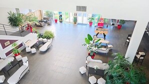 Um hall amplo com várias áreas de estar, plantas em vasos e uma grande janela que oferece iluminação natural.