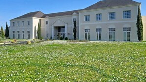Um edifício grande de dois andares, com fachada simétrica, entrada central e um gramado bem cuidado com flores brancas.
