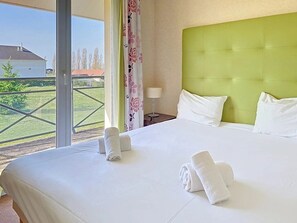 Camera d'albergo con un letto grande, una testiera verde, biancheria bianca e vista su un prato verde e un edificio.