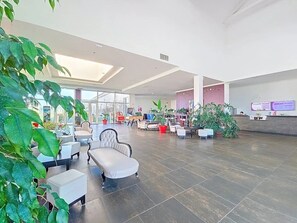 Een ruime lobby met zitgedeeltes, potplanten en een receptiebalie.