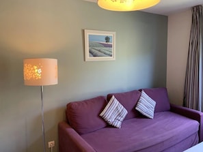 A room with a purple sofa, striped pillows, a floor lamp, and a framed picture on the wall. - Appartement 3 étoiles - Piscine  - ccbgefa (Gréoux-les-Bains)