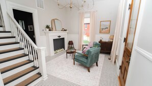 A staircase with white balusters, a fireplace with a mirror above, a teal armchair, and a patterned rug.