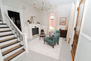 A staircase with white balusters, a fireplace with a mirror above, a teal armchair, and a patterned rug.