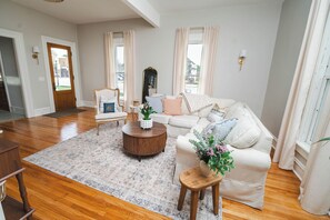 A living room with a wooden floor, a beige sofa, a round coffee table, and a small wooden side table with a vase of flowers.