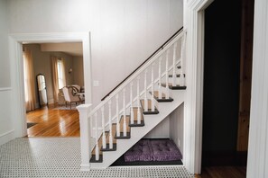 A staircase with white balusters and dark steps, leading to a room with a wooden floor and a purple cushion.