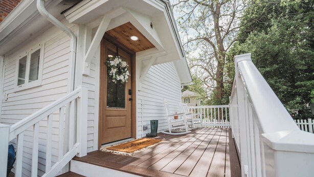 A white house with a wooden front door, a porch with a white railing, and a wooden staircase leading to the door. - Charming Restored Historic 3BR Home - The Larrabee (Williamston)